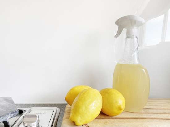 Lemons next to a spray bottle with lemon juice, a DIY cleaner that should be avoided for hardwood floors